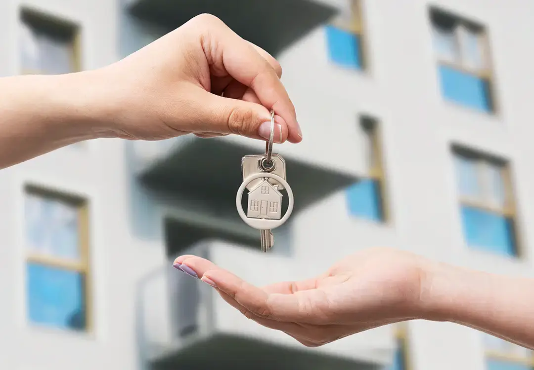 Zwei Hände halten einen Schlüssel zu einer Wohnung, symbolisieren den Besitz eines neuen Zuhauses.